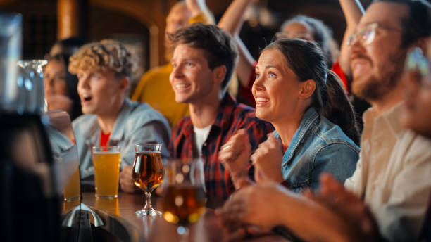 istock Group of Diverse Friends Cheering for Their Team, Drinking Beer at a Pub Counter. Supportive Fans Cheering, Applauding and Shouting. Joyful Friends Celebrate Victory After the Goal. 1481874087