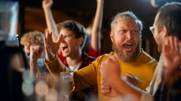istock Soccer Club Members Cheering for Their Team, Playing in an International Cup Final. Supportive Fans Sitting in a Bar, Cheering, Raising Hands and Shouting. Friends on a Night Out in a Pub. 1481875263