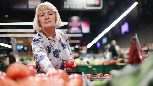Mature woman in casual clothes walking in mall and taking tomatoes and cucumbers