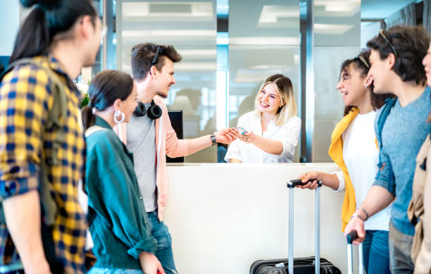 Young millenial friends having fun time at hotel reception desk on check in time - Travel life style concept with happy people waiting at guesthouse desk on fancy vacation - Bright vivid filter stock photo