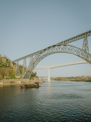 Douro river with traditional sailing wine boat cruise, view of Maria Pia and Sao Joao bridges, typical architecture of cascade housing in sunhine. Rabelo boat in douro river, Porto, Portugal