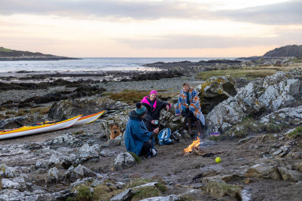 Bonfire at the Beach A group of friends enjoying a recreational weekend together in Dumfries, Scotland. They are having a rest with their dog around a handmade campfire on a beach in warm clothing and blankets after being in the sea. One man is toasting marshmallows over the fire. beach fire scotland stock pictures, royalty-free photos & images