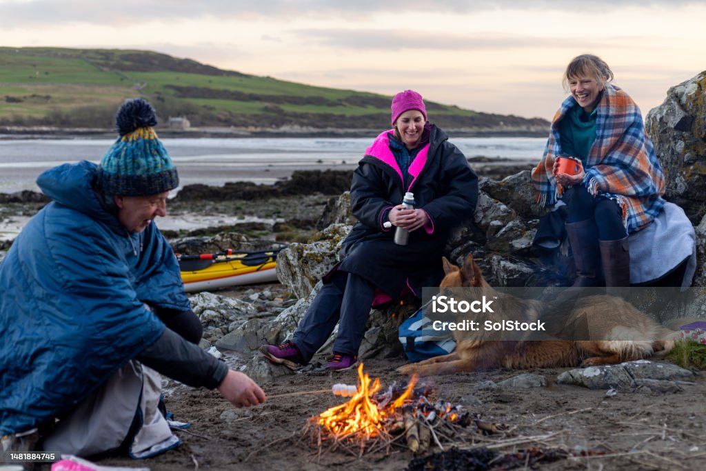 Taking a Well Deserved Rest A group of friends enjoying a recreational weekend together in Dumfries, Scotland. They are having a rest with their dog around a handmade campfire on a beach in warm clothing and blankets after being in the sea. One man is toasting marshmallows over the fire. Marshmallow Stock Photo