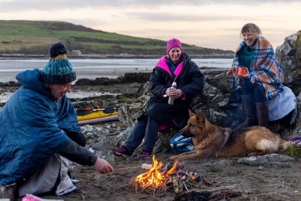 Taking a Well Deserved Rest A group of friends enjoying a recreational weekend together in Dumfries, Scotland. They are having a rest with their dog around a handmade campfire on a beach in warm clothing and blankets after being in the sea. One man is toasting marshmallows over the fire. beach fire scotland stock pictures, royalty-free photos & images