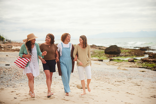 Mature group of women talking and laughing while walking together along a beach