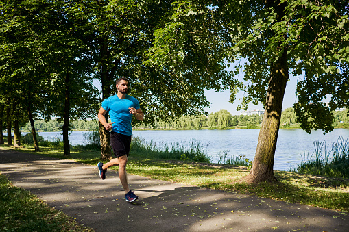 Man running in park during sunny summer day in public park