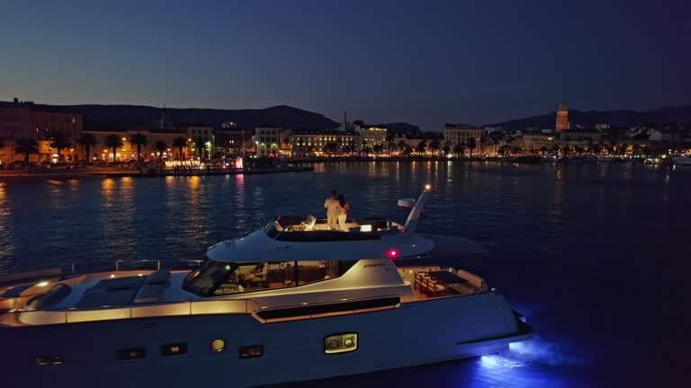 AERIAL Couple enjoying a drink on a yacht and view of a coastal town at night