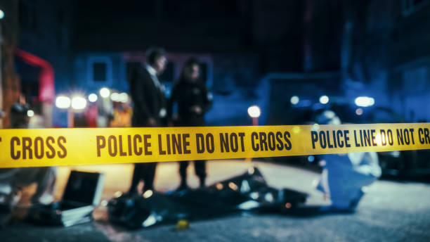 close up on crime scene yellow tape showing text police line do not cross. restricted area to the public. police on duty in the background. cinematic bokeh effect with red and blue neon lights - csi imagens e fotografias de stock