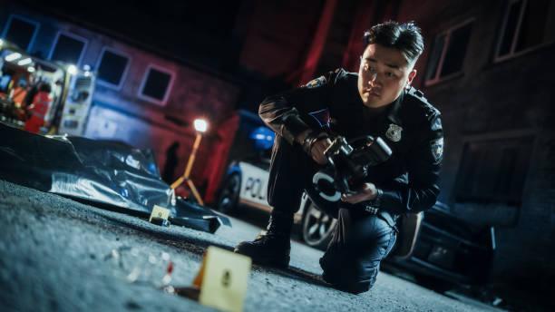 portrait tilted shot of male asian police officer taking forensic photos of evidence found next to the victim's bagged body on a crime scene. policeman archiving hit and run car accident evidence. - hit and run imagens e fotografias de stock