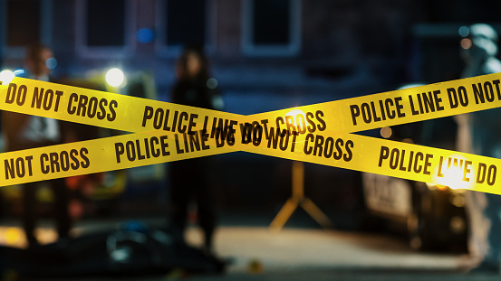 Restricted Area: Yellow Tape Showing Text Police Line Do Not Cross. Blurred Background with Crime Scene Investigation Squad Working on a Murder Case at Night. Cinematic Aesthetic Shot