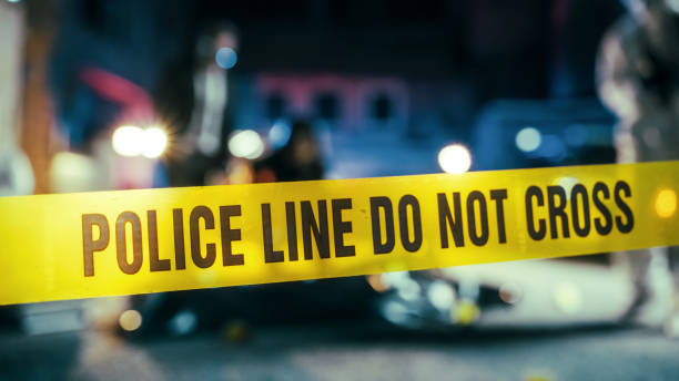 Yellow Tape Showing Text Police Line Do Not Cross Restricting a Crime Scene Area At Night. Close Up Aesthetic Shot with Bokeh Effect and Flickering Lights. Criminal on the Loose Strikes Again