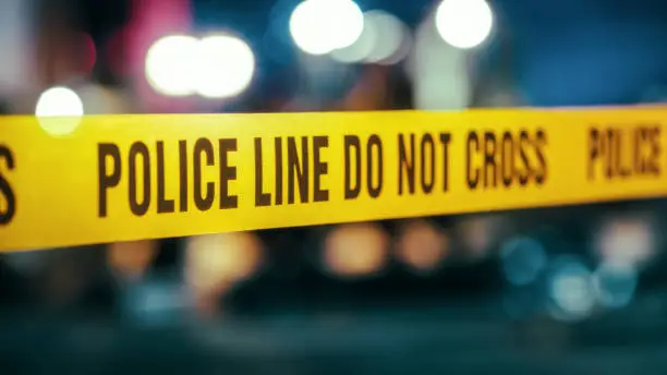 Photo of Yellow Tape Showing Text Police Line Do Not Cross Restricting a Crime Scene Area At Night. Close Up Aesthetic Shot with Bokeh Effect and Flickering Lights. Criminal on the Loose Strikes Again