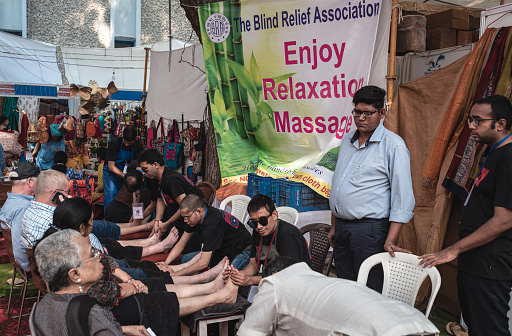 New Delhi, Delhi, India - 10.21.2019: A group of blind men from the blind relief association offering foot massage to people at an Indian festive fair known as the Diwali Mela for hindu festival.