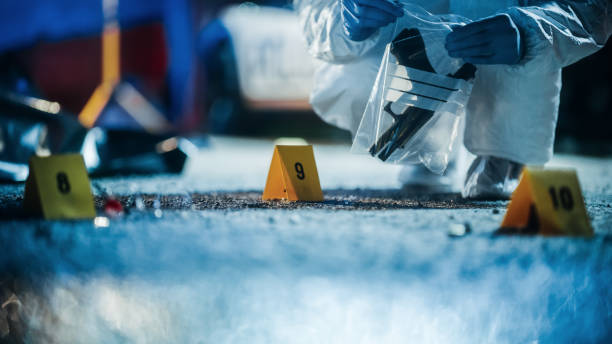 expert in coveralls starting packing evidence on crime scene after a tragic ending of a violent street fight. empty handgun identified as the murder weapon used to shoot the victim is found on spot - csi imagens e fotografias de stock