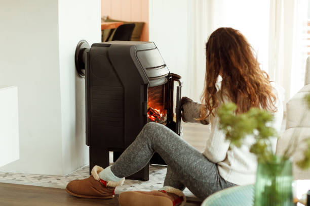 Woman sitting near fireplace at home, warming hands after winter walk in frosty weather Back view photo of brunette woman sitting near fireplace at home, female warming hands after winter walk in frosty weather. People and winter holidays concept wood burning stove stock pictures, royalty-free photos & images