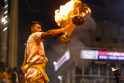 Varanasi, Uttar Pradesh, India - November 2022: Ganga aarti, Portrait of an young priest performing river ganges evening aarti at dasaswamedh ghat in traditional dress with rituals.