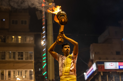 Varanasi, Uttar Pradesh, India - November 2022: Ganga aarti, Portrait of an young priest performing river ganges evening aarti at dasaswamedh ghat in traditional dress with rituals.