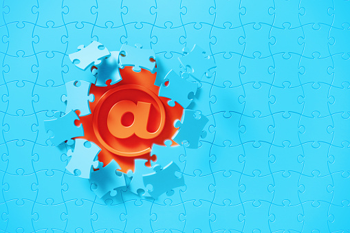 Blue jigsaw puzzle pieces revealing at symbol on orange background. Horizontal composition with copy space. Solution concept.