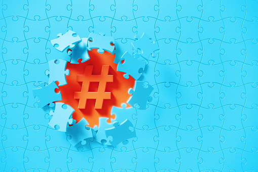 Blue jigsaw puzzle pieces revealing a hashtag symbol on orange background. Horizontal composition with copy space. Solution concept.