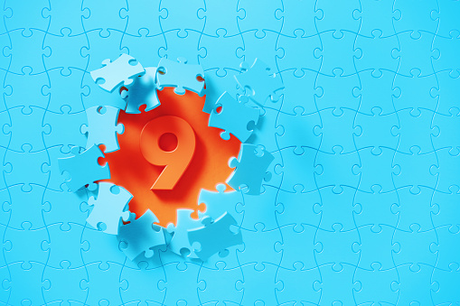 Blue jigsaw puzzle pieces revealing number 9 on orange background. Horizontal composition with copy space. Solution concept.