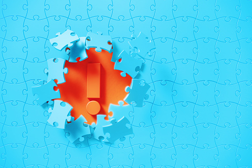Blue jigsaw puzzle pieces revealing an exclamation point on orange background. Horizontal composition with copy space. Solution concept.
