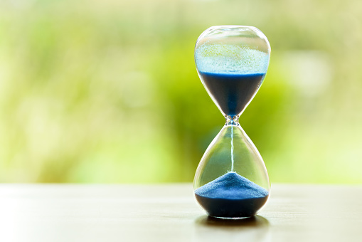 Hourglass with blue sand against a green background