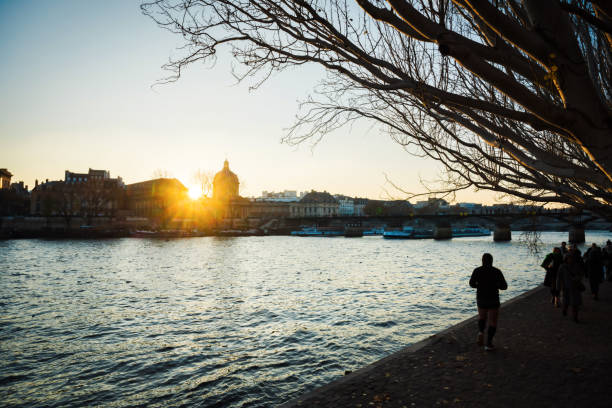 2019 People in Paris on the embankment. They are walking beside the River Seine with late afternoon winter sun. Paris, France.