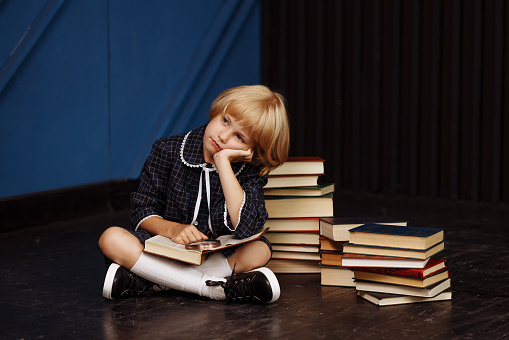 A schoolgirl is sitting surrounded by textbooks with a sad expression on her face.The concept of childrens problems in school, stress, homework. For projects about motivating and encouraging students.