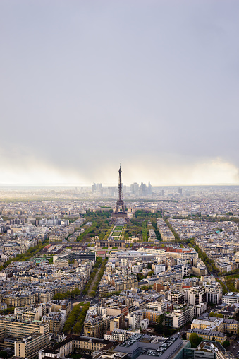 High view Paris cityscape, Eiffel Tower, Champs de Mars, and La Defense, evening with heavy clouds.