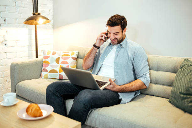 istock Man is sitting on a sofa and talking on a mobile phone 1481932127