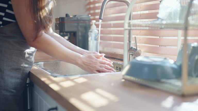 Close-up of Caucasian young adult woman washing dishes in the kitchen after finishing to enjoy breakfast with her girlfriend.