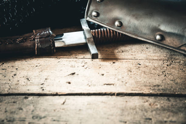 Close-up of an ornate medieval knight’s helmet with a visor, flanked by two swords. Historical armor displayed during a reenactment, perfect for illustrating medieval warfare, knightly traditions, and historical weaponry.