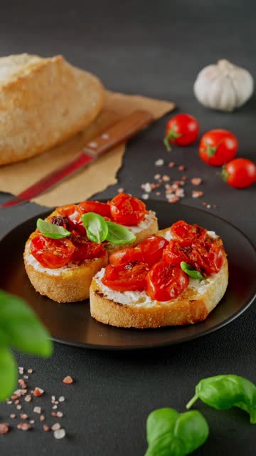 Bruschetta with Ricotto cheese and cherry Tomatoes, Basil, garlic on a black background. Food background. Vertical video