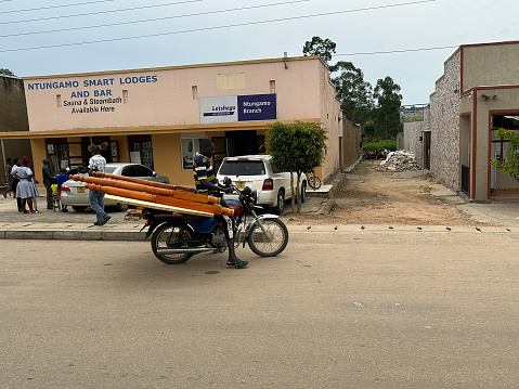 Ntungamo, Uganda, Africa - March 25, 2023: Typical roadside market scene, as a man hauls a bed frame on a motorbike boda boda