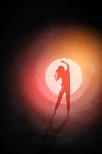 A conceptual image of a woman's silhouette in a dark tunnel of light being drawn toward an opening with ominous red light.