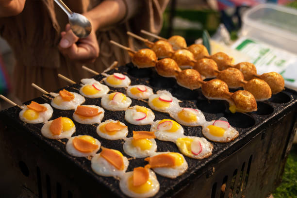 Fried Quail eggs in bamboo skewers on pothole pan. Drop each egg in a small ramekin gently slide it into the hot oil. Serve warm with salt and ground pepper. Thai appetizer at street food market. huevos de codorniz fritos en brochetas de bambú en una sartén con baches. deja caer cada huevo en un pequeño ramekin y deslízalo suavemente en el aceite caliente. servir caliente con sal y pimienta molida. aperitivo tailandés en el mercado de comida c