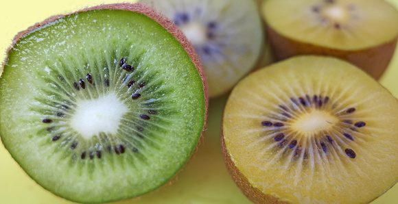 Sliced kiwis on a yellow cutting board. The yellow one is called Actinidia chinensis or golden kiwifruit. The green one is called Actinidia deliciosa or fuzzy kiwifruit
