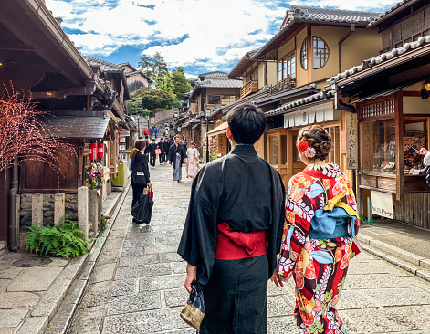 Young Japanese couple dressed in Yukata traditional dresses walk holding hands in popular Ninenzaka alley in Higashiyama-ku ward lined with old houses