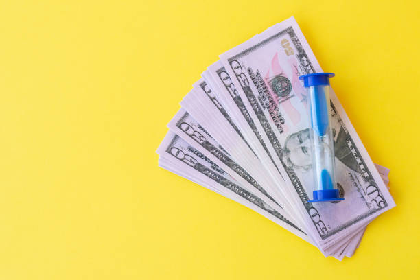 istock Sand watches with american dollar banknotes on yellow background. 1481964263
