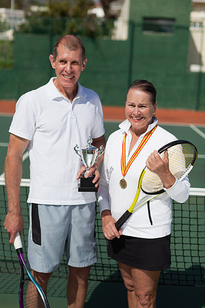 coppia più anziana con il trofeo sul campo da tennis - tennis court love victory foto e immagini stock