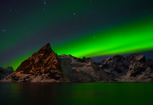 Strong Aurora borealis dancing behind and over mountains on Lofoten islands in Norway.