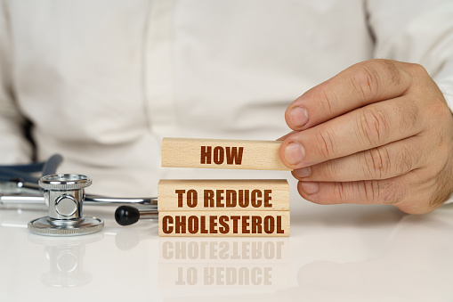 On a white surface, a stethoscope and wooden plates with the inscription - How to Reduce Cholesterol