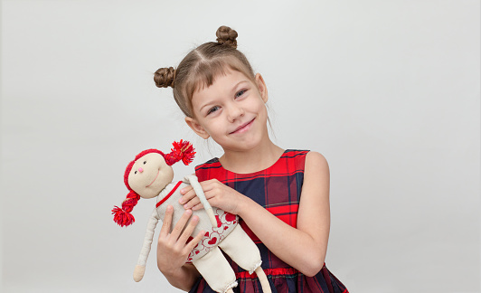 Happy and smiling child hugging doll toy on white background caucasian little girl kid of 6 7 years in red plaid dress looking at camera