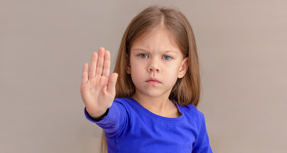 Child showing hand as sign to stop focus on kid, isolated on white background looking at camera waist up caucasian little girl of 5 years in blue