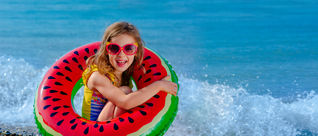 Beach holidays in summer on the seashore. A child with an inflatable ring. Children swim. An insurance event. Safe rest with a child on the water. Storm warning. Rescue of drowning people. Tourist offer.