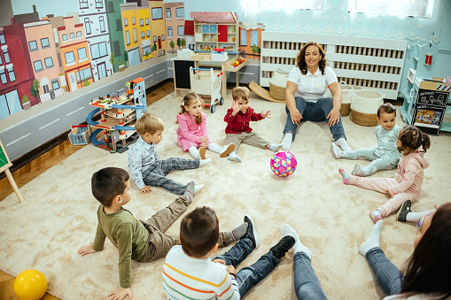 Preschoolers sitting on the floor of the classroom listen to the teachers telling stories.