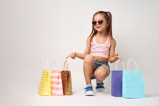 Cute little girl with shopping bags on a white background with copy space. Portrait of a child girl with colorful shopping bags, full body