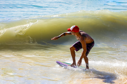Playa del Carmen, Mexico - March 12, 2023: Man enjoying his skimboarding of the waves on the shores of the Caribbean Sea, which consists of surfing the waves with a board smaller than a surfboard.