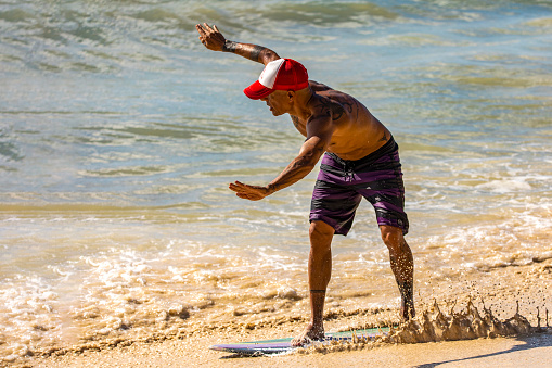 Playa del Carmen, Mexico - March 10, 2023: Man practicing skimboarding which is a modality that is practiced on the shore and that consists of surfing the shore waves with a smaller and thinner board.