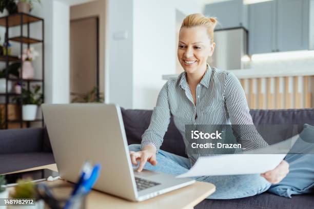 Mature Entrepreneur Working From Home On Laptop Anaylzing Documents And Doing Paperwork Stock Photo - Download Image Now